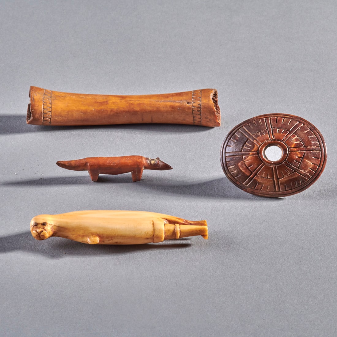 A collection of Eskimo artifacts: Alaska, 19th century and earlier, a bone needle case with banded decoration at both ends, a fox, a toggle with incised decoration on the front and pierced in the center with lug behind, likely Thule p