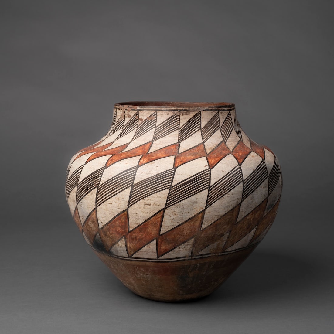 An Acoma polychrome jar: Decorated with a twisted geometric design in black fine lines on a natural ground, (rim loss and a crack from rim). Ht. 11, wd. 11 ¼ in. Provenance: Private collection, Santa Fe, New Mexico.