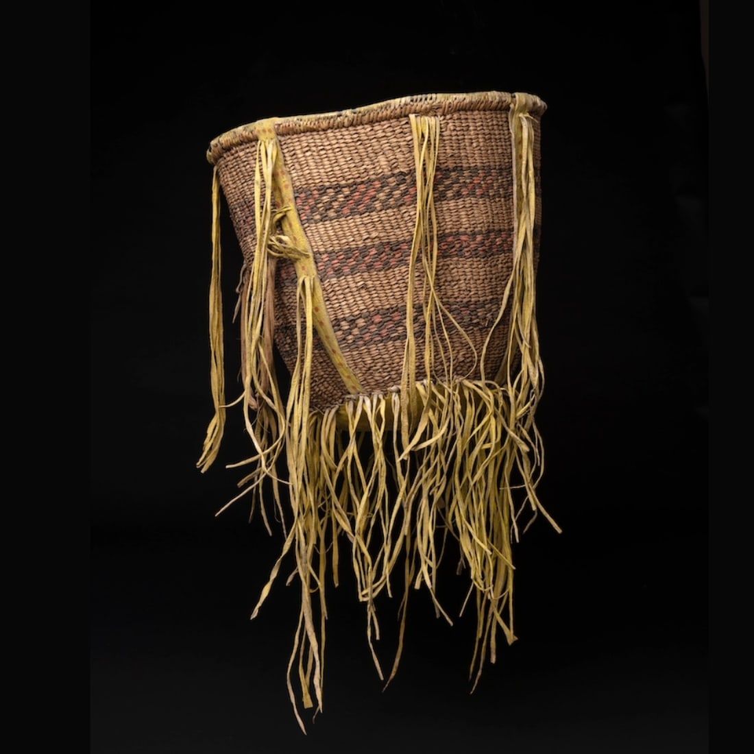 A pigmented Southwestern burden basket: Apache, 19th century, the rim reinforced with heavy wire, decorated with three checkered bands, the side straps and bottom hide, with yellow over pigment with red dots, with fringes. Size of basket no