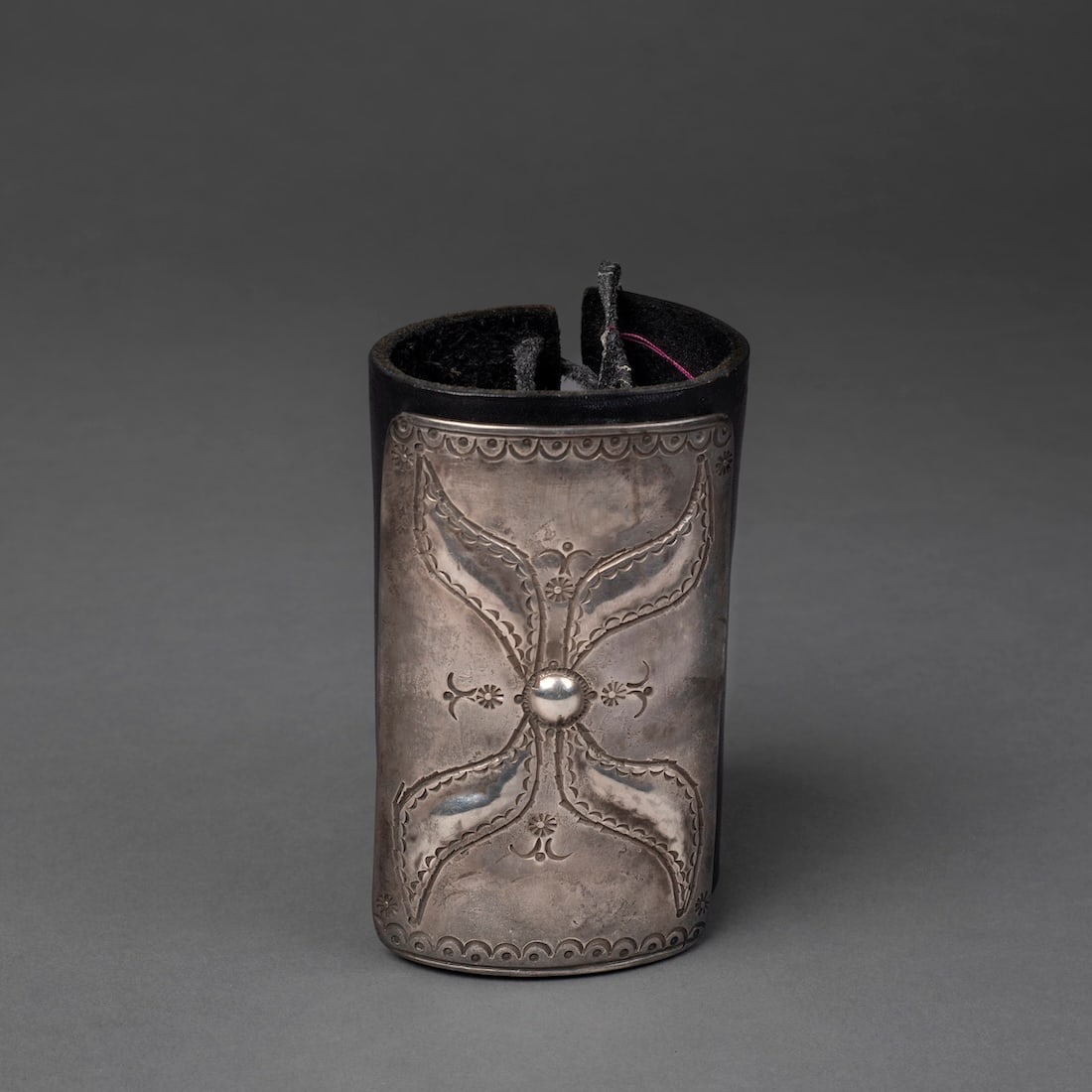 A Navajo (Diné) silver bow guard, Ketoh: The heavy silver plaque with repoussé work, chisel and stamp decoration, attached to a contemporary leather wrist band. Size of plaque 4 1/8 x 2 1/2 in.