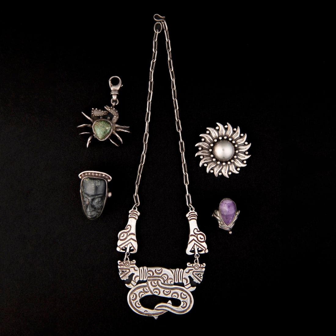 A collection of Mexican jewelry: A Pre-Columbian style silver necklace marked, "Mexico 980," two rings, one with a blue stone, the other with a stone head marked, "Los Castillo Sterling Made in Mexico," a crab pendant marked, "Love,"