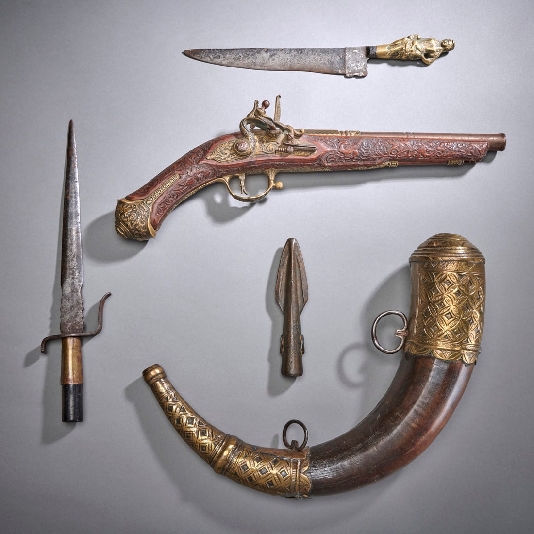 Five European Weapons: Circa 19th century, a profusely decorated flintlock pistol, a powder horn, two daggers and a possibly ancient spear head. Generally good condition. Lg. of pistol 16 in. Shipping within the continental