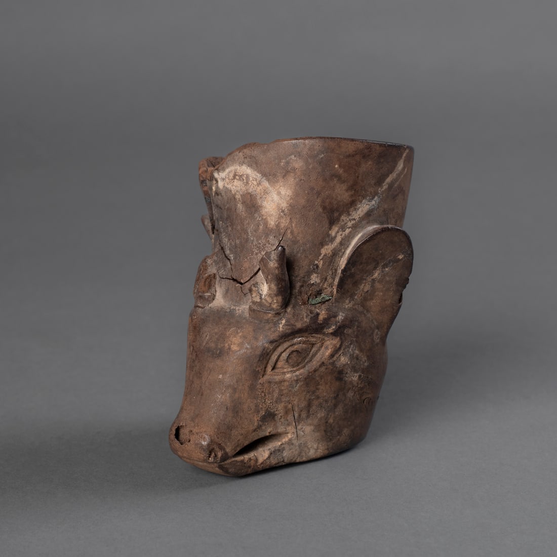 A wood Kero in the form of a deer head: Carved in the likeness of a deer, with elongated snout, incised nostrils, and applied ears. The vessel rises from the animal’s head, showing age cracks and surface wear. Dark patina overall. Ht. 4 &