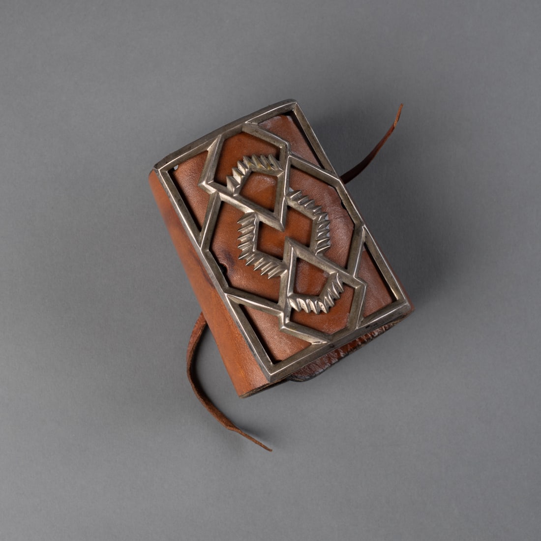 A Navajo (Diné) ketoh: Featuring a geometric overlay design in silver set over a leather strap. Ht. 4 ¼ in.