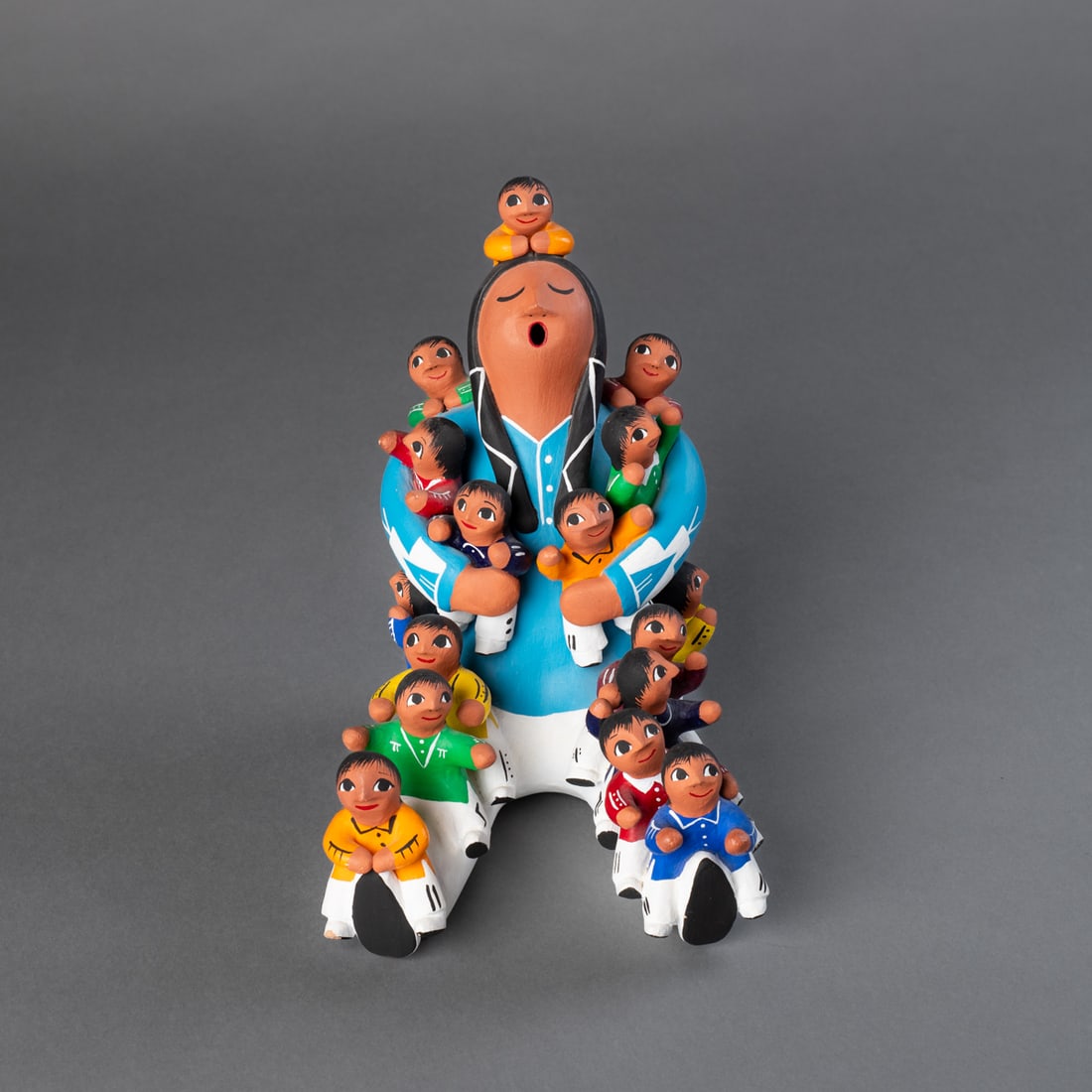 An Alma Loretto storyteller figure: Brightly painted polychrome pottery storyteller featuring 16 children atop grandmother. Each child is individually detailed with various colored outfits. The grandmother has long braids and wears a tu
