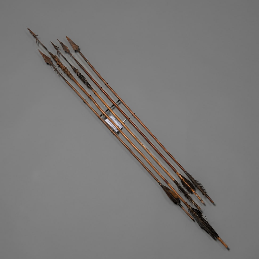 Group of Early Philippine handmade arrows: Five arrows, each exhibiting unique craftsmanship, forged with metal points and distinct wrapping patterns. Feathers featured at the bases. 19th century Retains an old brass identification tag from