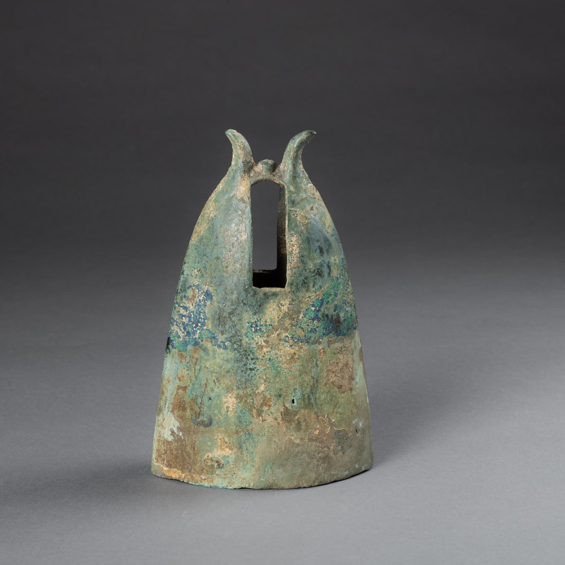 A Vietnamese bronze bell: The bell with wide oval opening rising to a graduated top with two spurs, with a rectangular slit either side at the top, encrusted patina. Ht. 7, wd. 4 in. Provenance: Private collection,