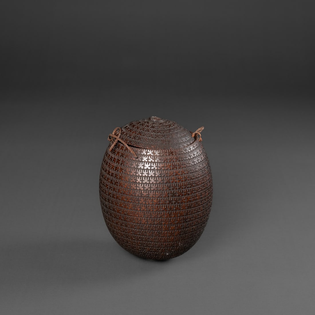 A Marquesan carved coconut vessel: Late 19th century, the coconut with lid, fully decorated with a repeated abstracted figure device, with broken sennit fiber attached at rim. Ht. 6 1/4, wd. 4 in. Provenance: Private collection, Los