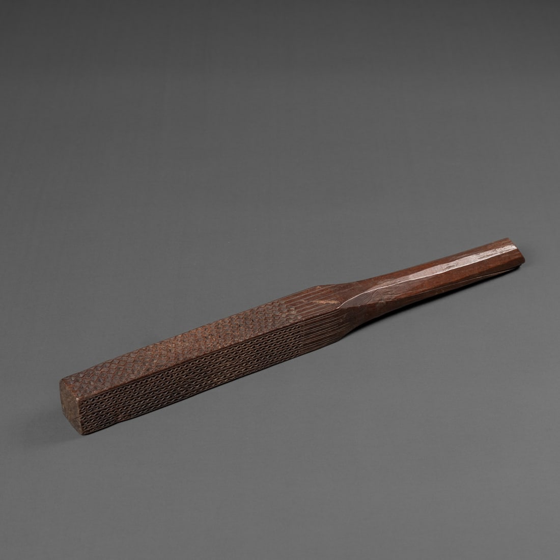 A Hawaiian kapa beater: Early 19th century, the rounded handle leading to a four-sided squared surface, each with a different incised pattern, an old label attached, (wood split to handle). Lg. 15 3/4 in. Provenance: