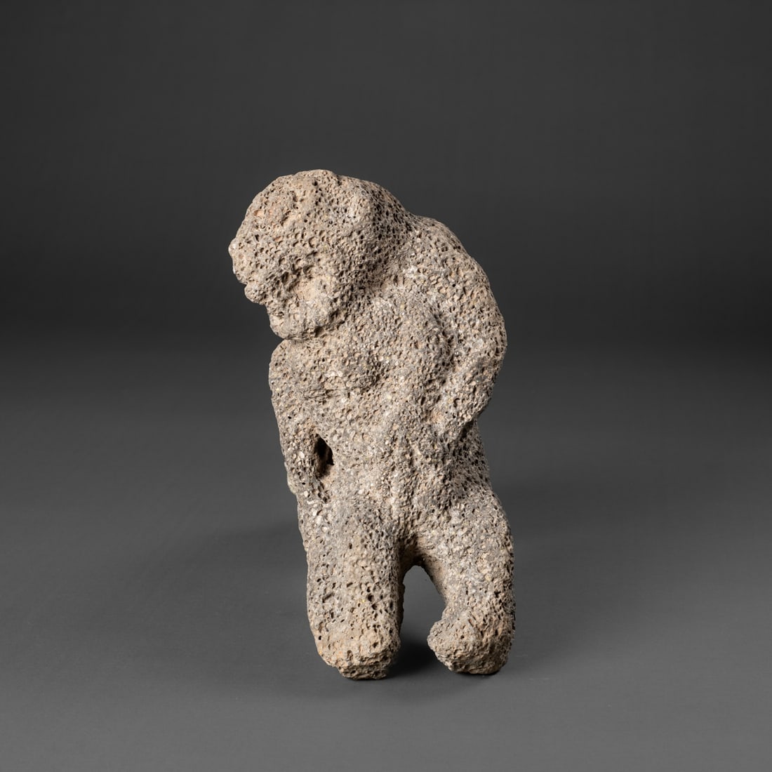 A Hawaiian stone figure: Carved from basalt, the abstract human figure with large, open mouth and round eyes and nose, breasts and the left arm with a three-fingered hand and legs below. Lg. 10 1/2 in. Provenance: Private col