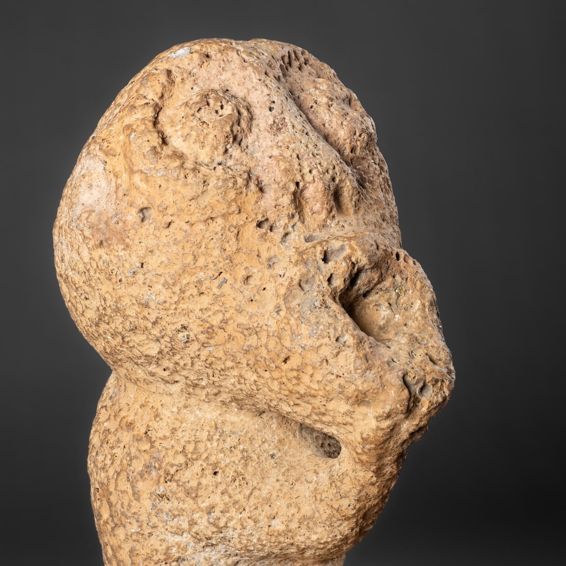 A Hawaiian stone figure: Carved from basalt, the abstract figure with large head and large open mouth, the right arm extended to support it, with legs drawn up. Lg. 12 3/4 in. Provenance: Private collection, Santa Fe, NM; The