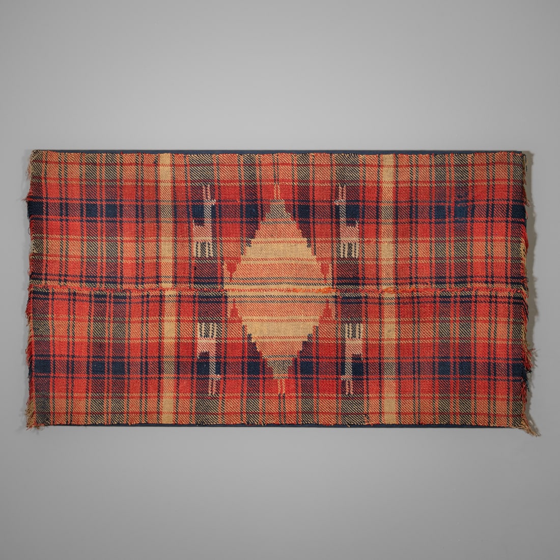 An early South American pictorial textile: 19th century, or earlier, the woven textile panel with a red and blue checked ground featuring a central stepped diamond motif in tan and rust tones. Handwoven in wool with visible selvedge and age fr