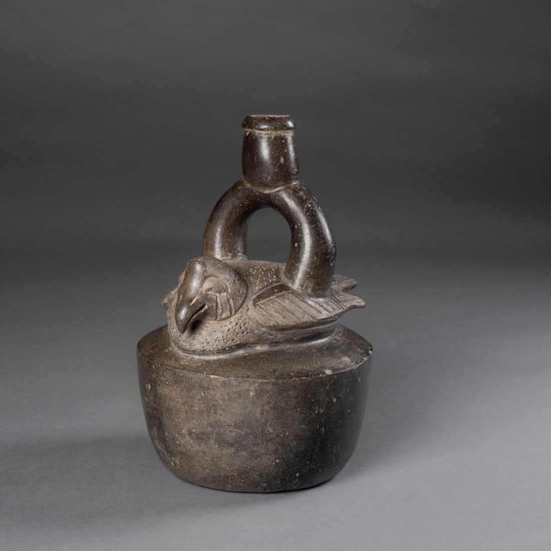 A Pre-Columbian stirrup spout vessel: Chavin, the flat bottom vessel with round body, with a molded bird above, with a stirrup spout from the bird's wings, overall black surface. Ht. 9 1/2, wd. 5 in. Provenance: Private collection, Phoeni