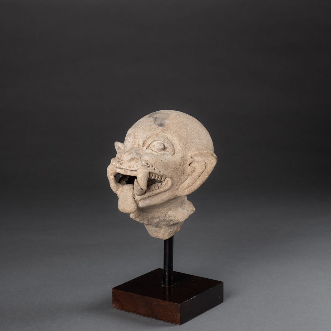A Pre-Columbian effigy ceramic head: La Tolita, Ecuador, circa 800 B.C-400 A.D., the ceramic jaguar transformation head, mounted on a custom stand, the tip of the tongue, lower right tooth, broken and restored. Ht. 4 3/4, wd. 5, lg. 4 7/