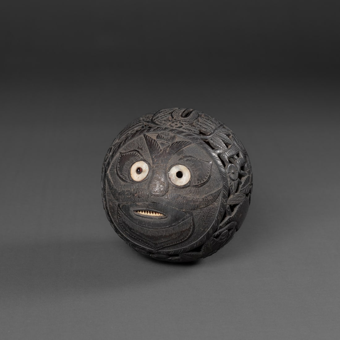 A Spanish colonial bugbear: 19th century, the fully carved coconut depicting Native Americans and colonial settlers, one end with foliate motifs and the other a face with eyes and mouth inlayed with shell. Lg. 4 1/, wd. 3 3/4 in