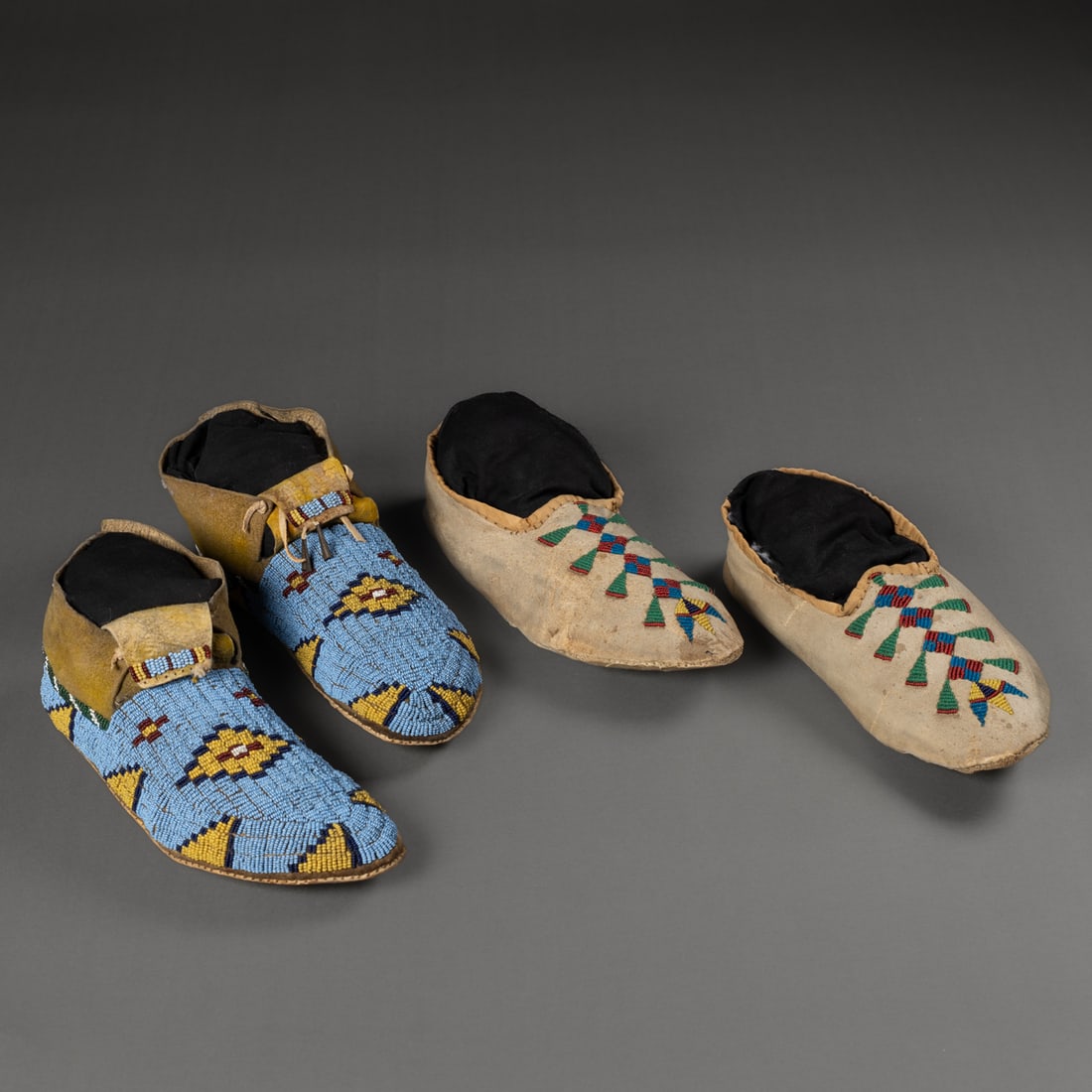 Two pair of Plains beaded moccasins: Late 19th century, the raw hide soles with fully beaded uppers in typical Plains motifs on a blue ground with beaded tongues, with a soft hide pair with raw hide soles and bead decorated vamps. Lg. 9