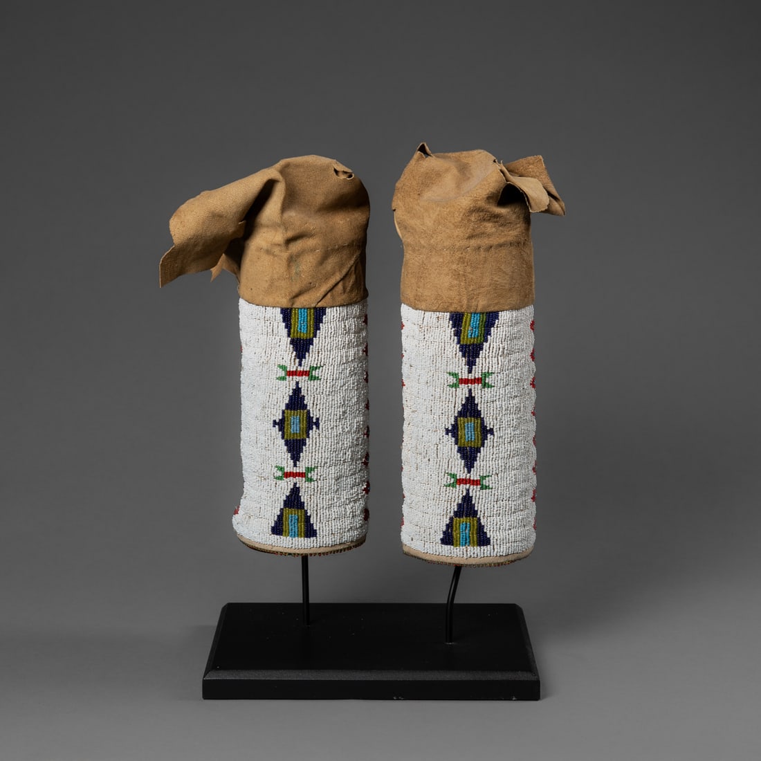 A pair of Plains beaded leggings: C. 1910, the soft hide legging with a wide band of beadwork, decorated in multicolored geometric designs, with beaded fringe at the bottom, (some tears in the hide at the top), mounted on a custom