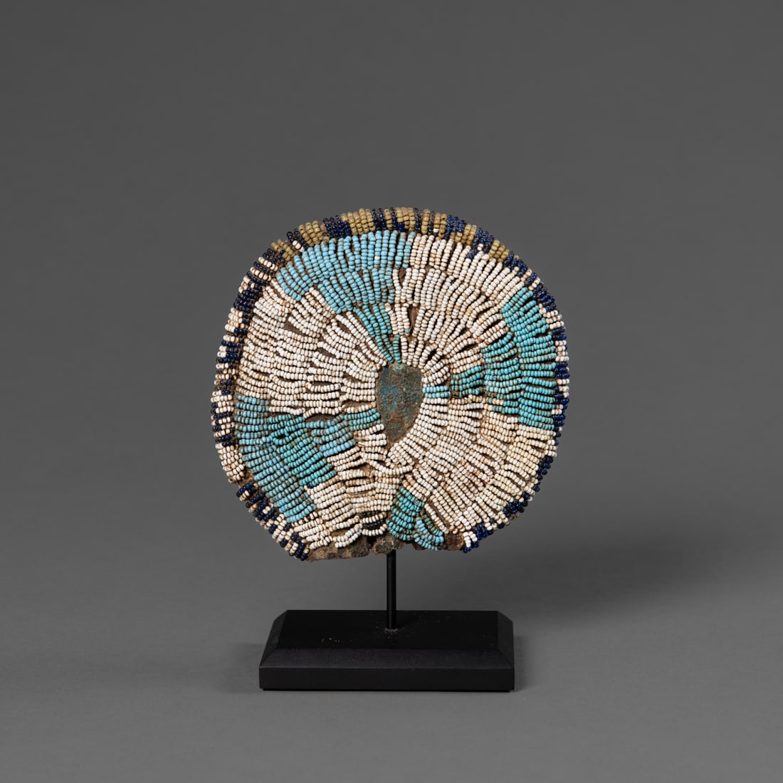 A Ute/Apache beaded circular pouch: Circa 1870s, the circular pouch consists of two pieces of native tanned hide sewn together with sinew, the front piece features a blue seed bead and Maltese cross on a white field, the center not