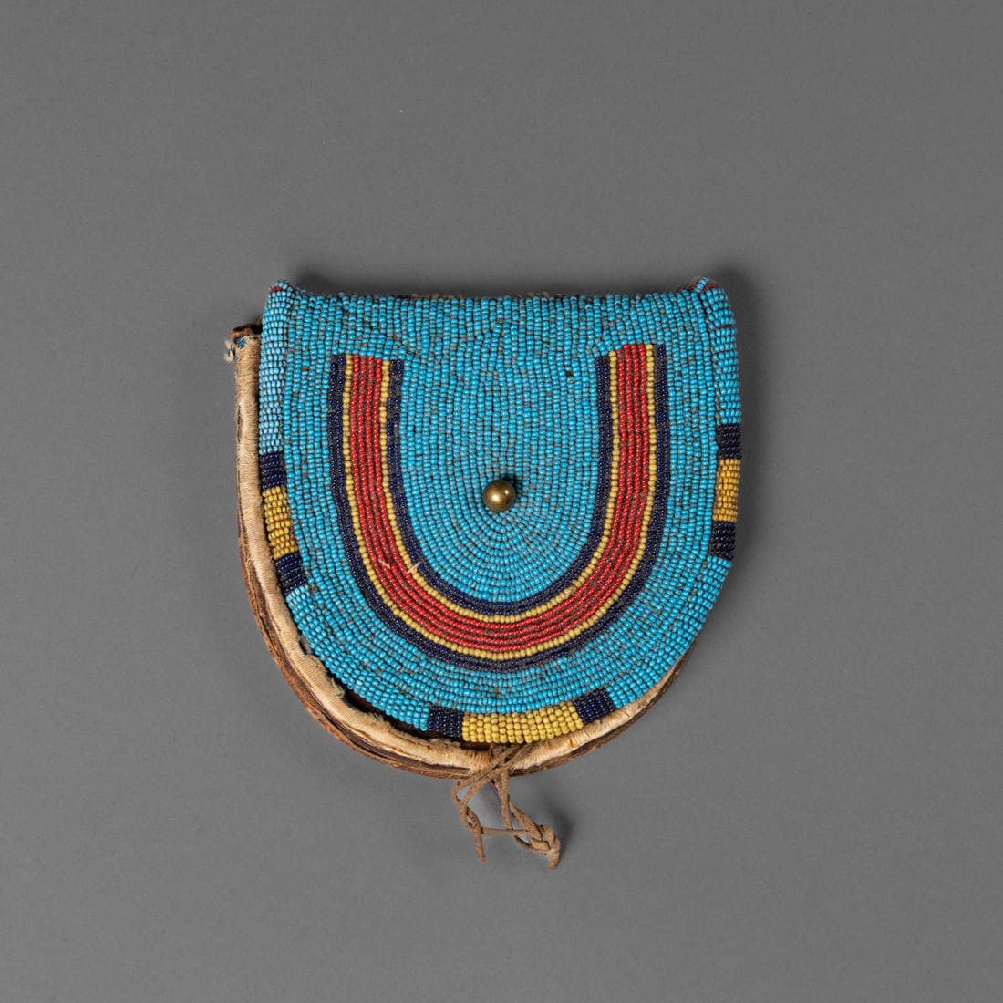 A Plateau beaded belt pouch: Third quarter 19th century, comprising commercial harness leather, the front decorated with a large horseshoe pictograph on a blue trade bead field. Ht. 5, wd. 5 1/8 in. Provenance: The James Pavitt