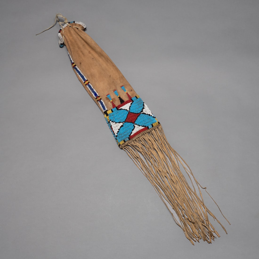 A Plains beaded hide tobacco bag: Arapaho or Cheyenne, circa 1880s, native-tanned hide with a beaded upper panel in geometric designs of red, white, light blue, and dark blue, with long twisted fringe and beadwork extending down the