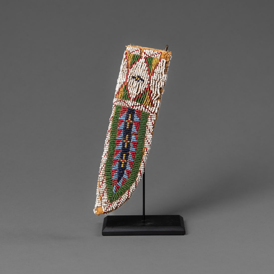 A double-sided Plains beaded knife sheath: Lakota, circa 1860s/early 1870's, a woman's double sided bead decorated knife sheath on native tanned hide, with buffalo hide parfleche liner, mounted on a custom stand. Lg. 7 in. Provenance: The