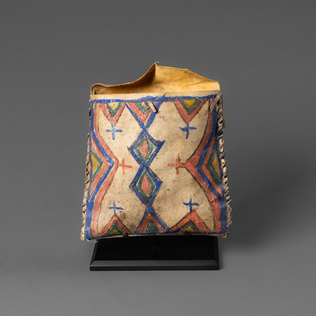 An Arapaho parfleche pouch: Fourth quarter 19th century, the square-shaped parfleche pouch decorated on both sides in multicolored diamond and triangle devices, the flap also painted, mounted on a custom base. Lg. 8, wd. 7 1/4