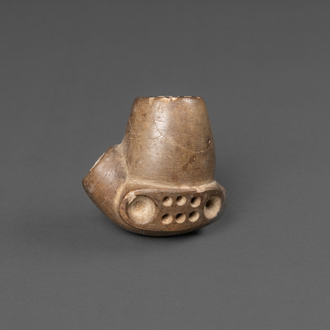 A Northern Plains Blackfoot pipe bowl: The stone pipe bowl, 19th century, likely Blackfoot, of dark brown stone, circular stem opening, deeply drilled. The upper surface features rounded nodes and incised lines surmounting the piece.