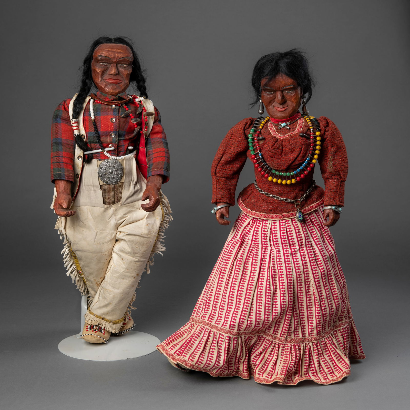 A pair of Navajo (Diné) wood dolls: Early/mid 20th century, large carved wood trading post dolls, with leather and colored bead moccasins, western clothing, each with custom-made Navajo-style jewelry. Ht. 24 in. Each.