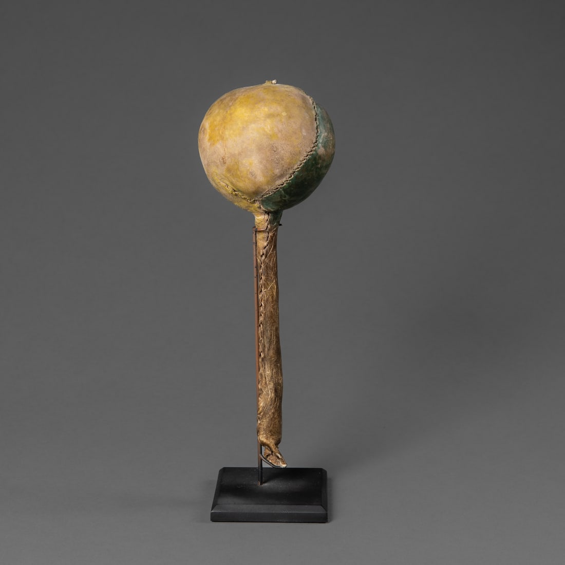 An Arapaho rattle: Circa 1870/80's, the rounded container rattle made from rawhide, filled with stones and attached to a wood handle, painted with green and yellow pigments, mounted on a custom stand. Ht. 11 1/2 in.