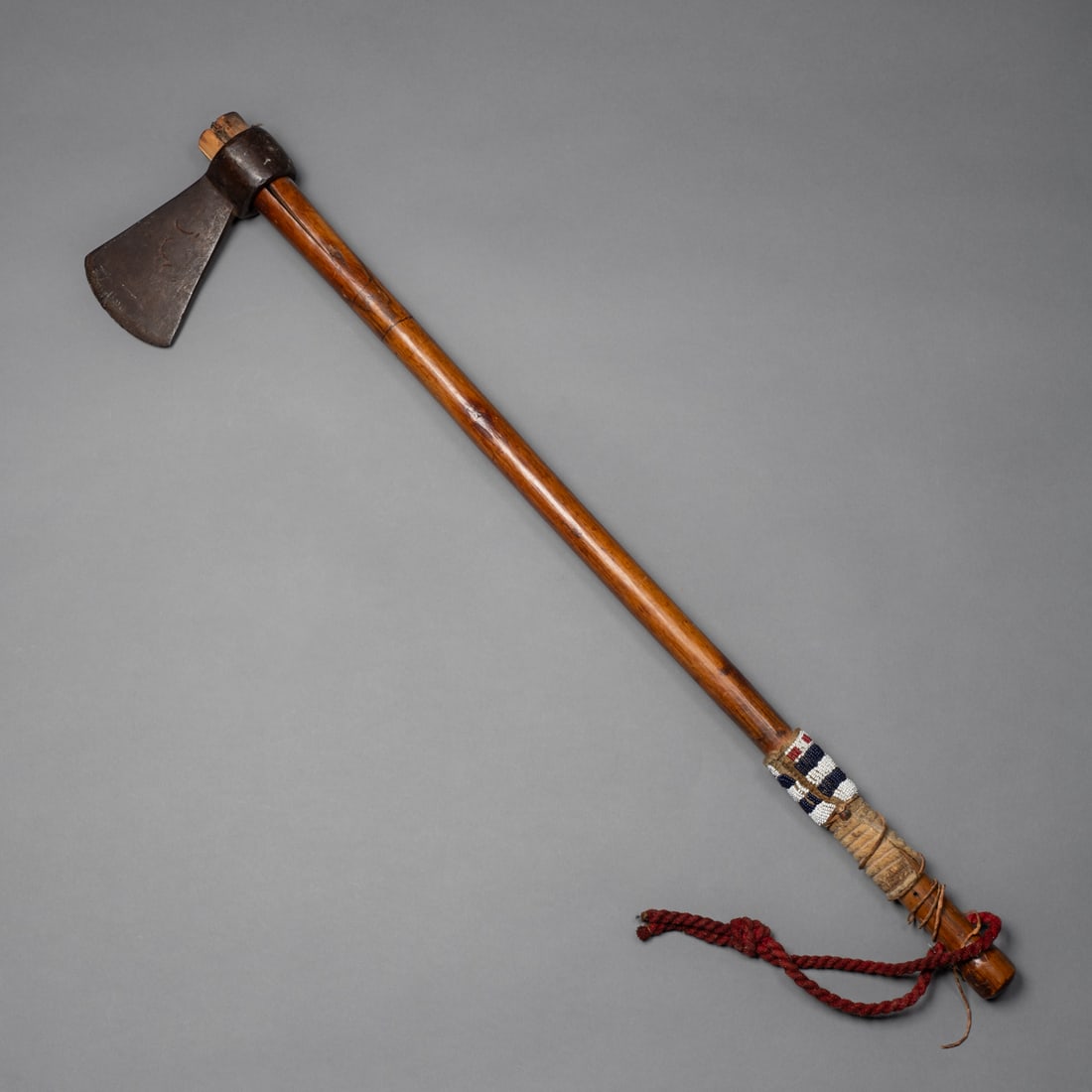 A Northern Plains trade axe: A 19th-century Northern Plains trade axe, with original haft and bead decoration adornment, featuring a forged iron head mounted on its original hardwood haft. The handle retains traditional Plains