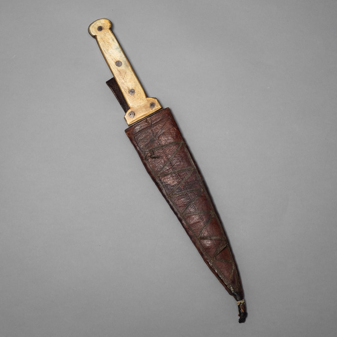 A Northern Plains, Western Great Lakes dag knife: A 19th-century Northern Plains or Western Great Lakes Indian dag knife, featuring a forged trade blade fitted with a carved handle secured by iron rivets. The knife retains its original, red-dyed hide