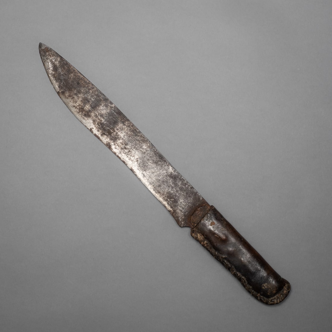 A Northern Plains knife with rawhide covered handle: The long sharp, skinner type trade blade with a time worn patina, attached to a smooth rawhide handle. The handle of a deep rich brown color and smooth hand feel, notched around the edges. Lg. 15 in.