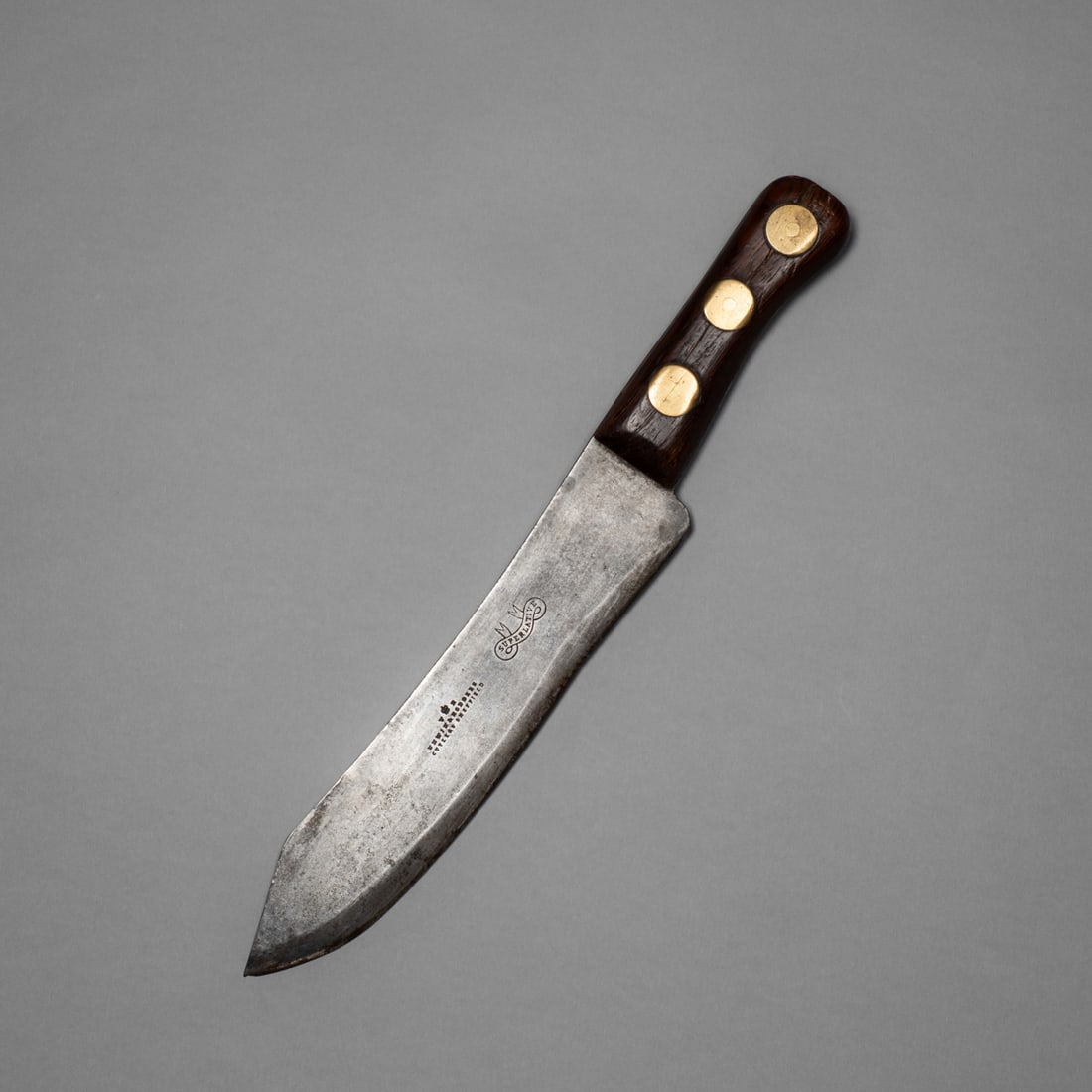 A heavy Northern Plains/fur trader camp knife: A camp knife with a long sharp blade featuring a dark hardwood handle secured by three large brass rivets. The blade has a squared point and is stamped “Unwin & Rodgers Cutlers, Sheffield” and