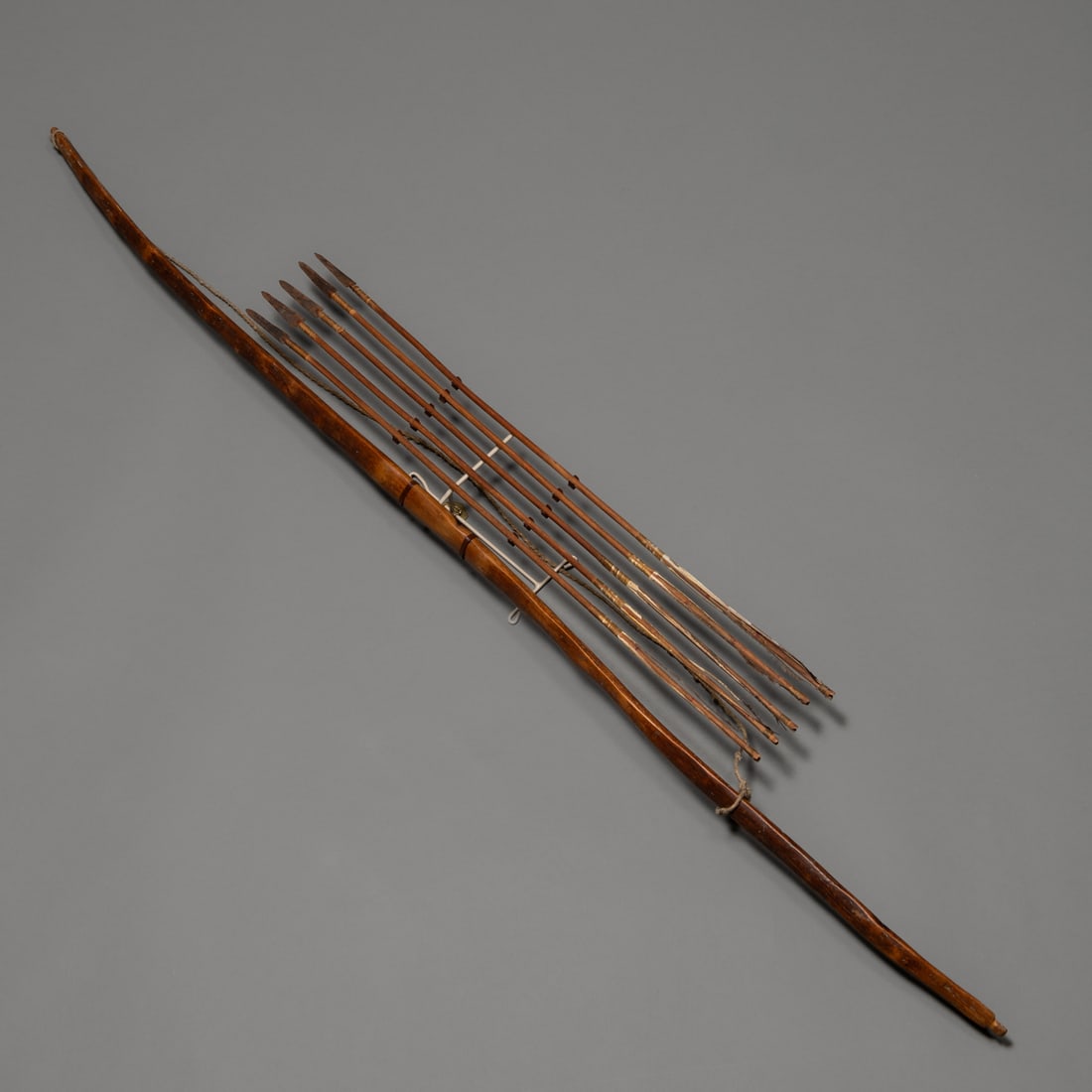 An Apache bow with five arrows: 19th century, with five arrows, the bow carved from a single piece of hardwood with a curved profile, with rich brown patina, the arrows with iron pointed, mounted on a custom wall mount. Lg. of bow 4