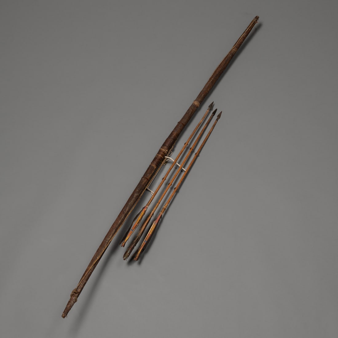 A Hopi bow with three arrows: 19th century, the curved bow with sinew-wrapped middle and ends, with sinew string and three iron-tipped arrows, mounted on a custom wall mount. Lg. of bow 49 1/2 in. With a brass collection tag marke