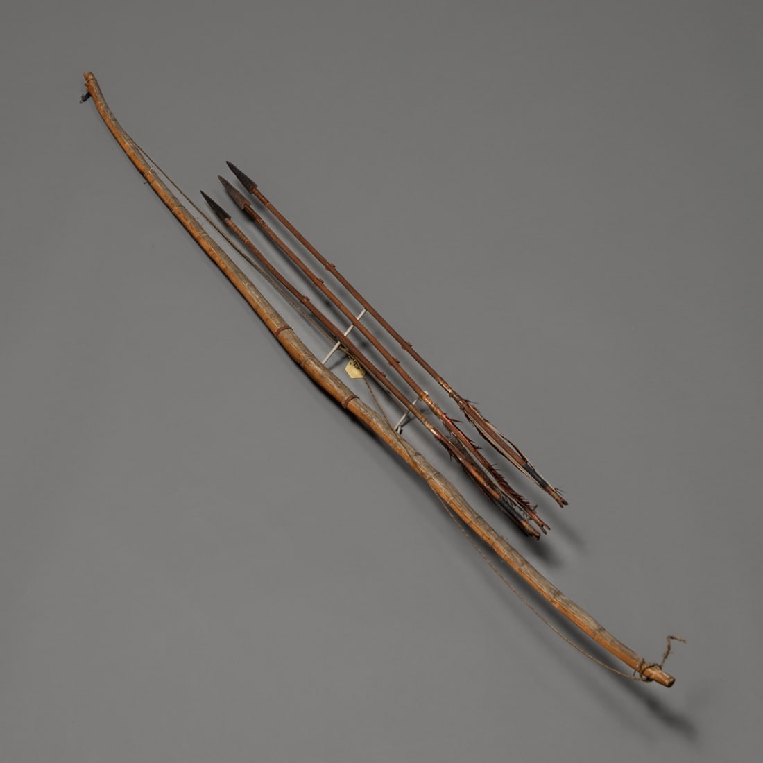 A Northern Plains bow with three arrows: 19th century, the curved bow with sinew-wrapped middle and ends, with sinew string and three iron-tipped arrows, mounted on a custom wall mount. Lg. of bow 46 in. With a brass collection tag marked ��