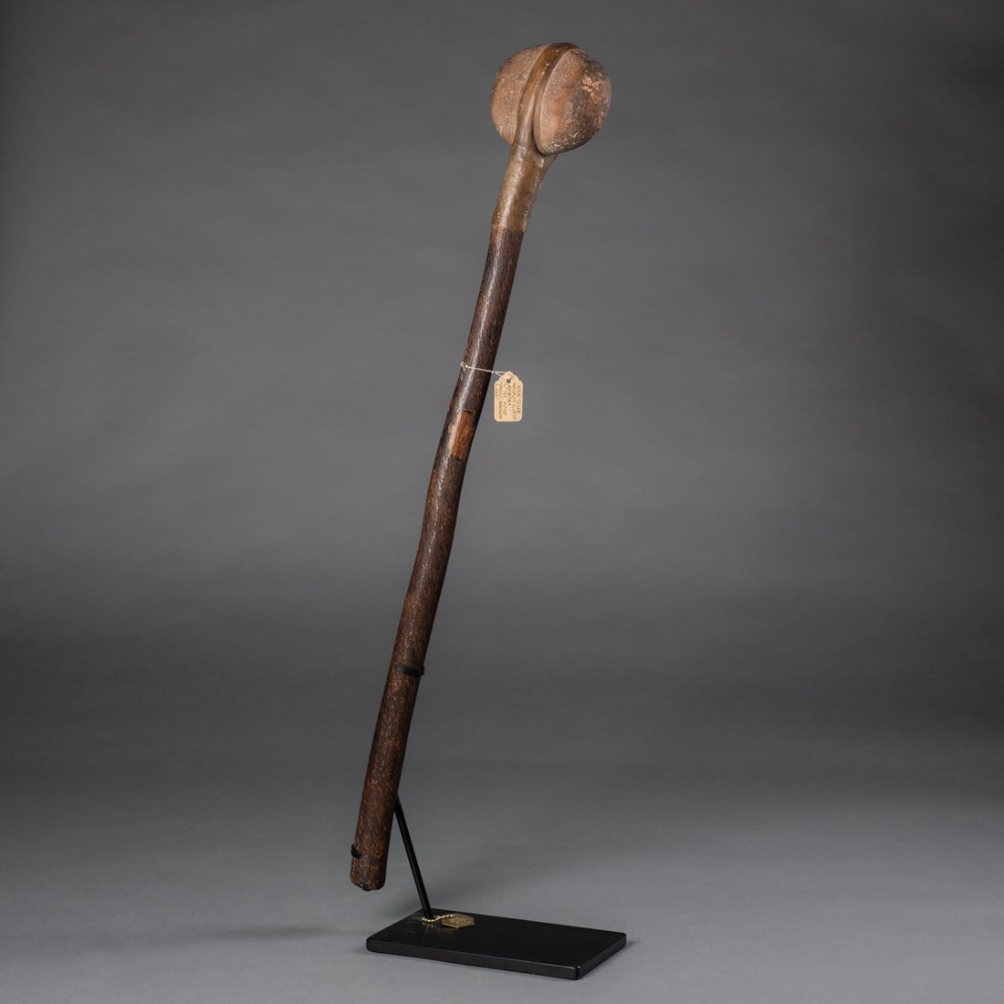 A Navajo (Diné) war club: 19th century, the long wood handle with smooth rounded stone head attached with rawhide, mounted on a custom metal stand. Lg. 26 1/2 in. Provenance: The Richard Corrow collection, Mesa, AZ. Inventory