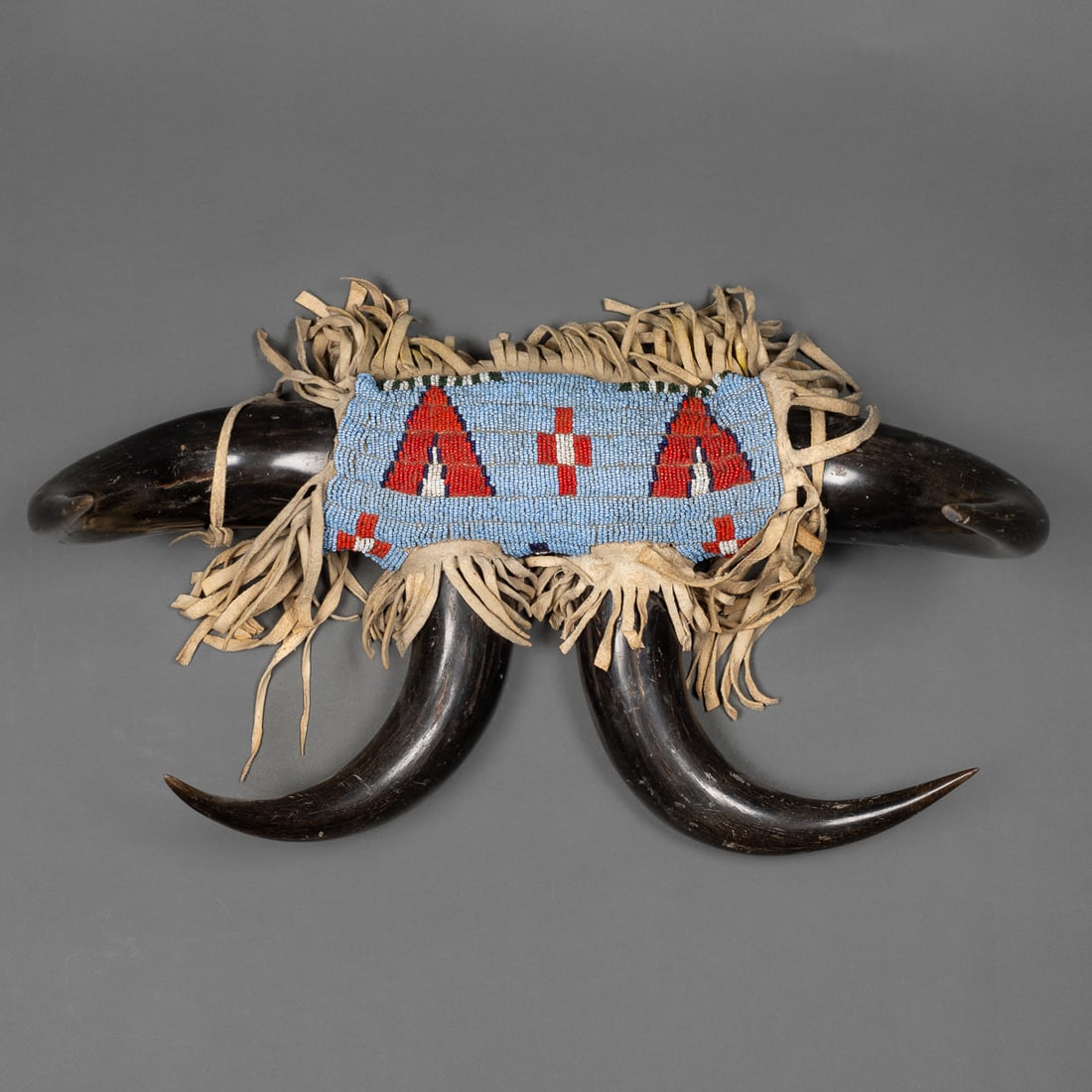 A bead decorated buffalo horn coat rack: Circa 1890’s, composed of four polished buffalo horns arranged symmetrically and joined at the center by a beaded hide panel. The beadwork, executed in classic Lakota style, features geometric tipi