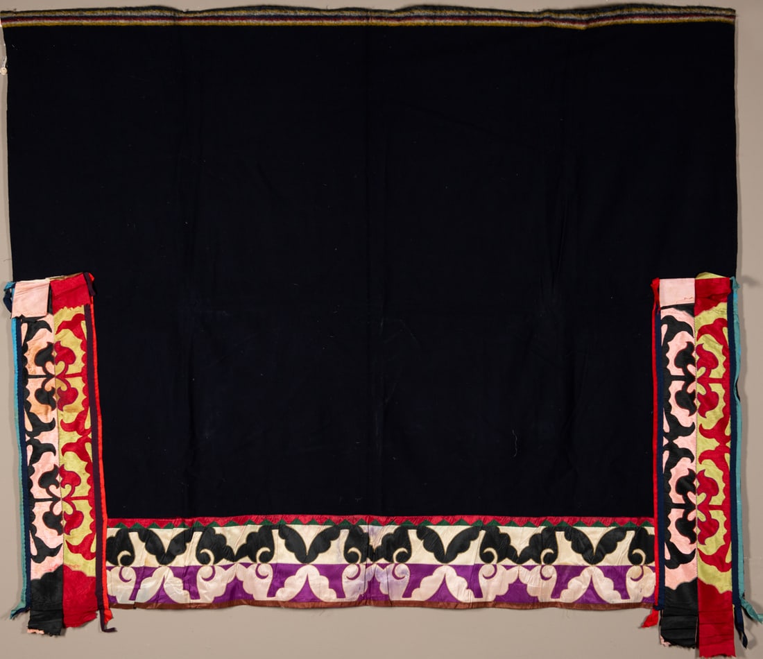 An important Menomonee ribbon work shawl: Composed of deep indigo-blue stroud cloth with original selvage edges and richly applied silk trade ribbon borders. Featuring symmetrical, curvilinear motifs of bold red, black, pink, yellow, and