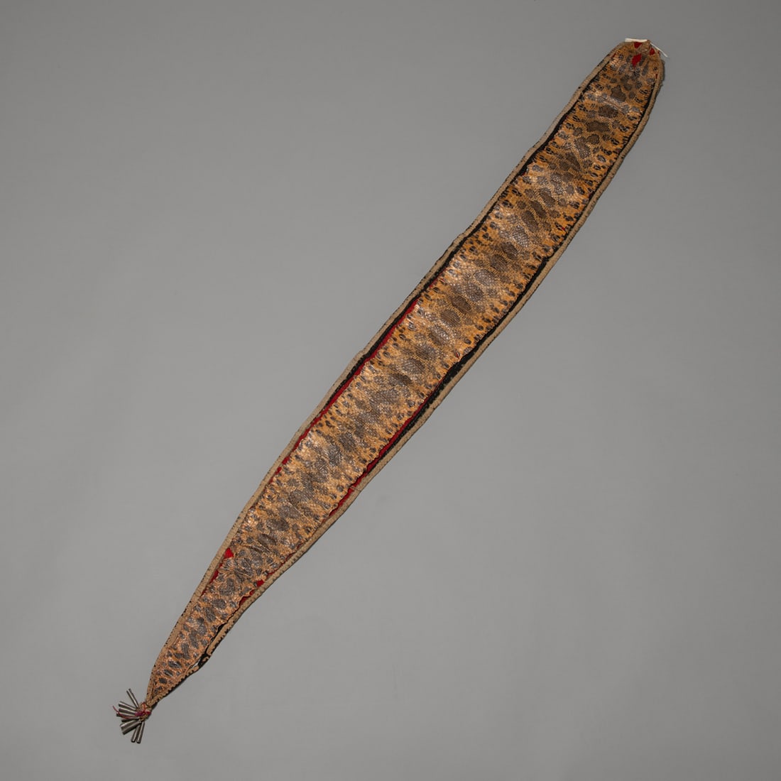 Woodland Indian Snake bandolier: Early to mid-19th century,Great Lakes Indian snake bandolier with skin mounted on black/blue and red wood trade cloth, tin cones adornments, worn silk ribbon edging. Size 62 by 6 1/2 in. Provenance: