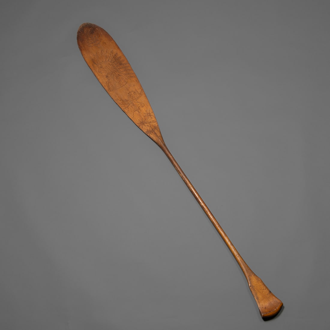 A Northeast Woodlands canoe paddle with carved designs: Penobscot, finely carved with traditional Penobscot imagery on each side including a maple leaf, a Native chief in profile wearing a feathered headdress, a moose head with antlers, and leaf and