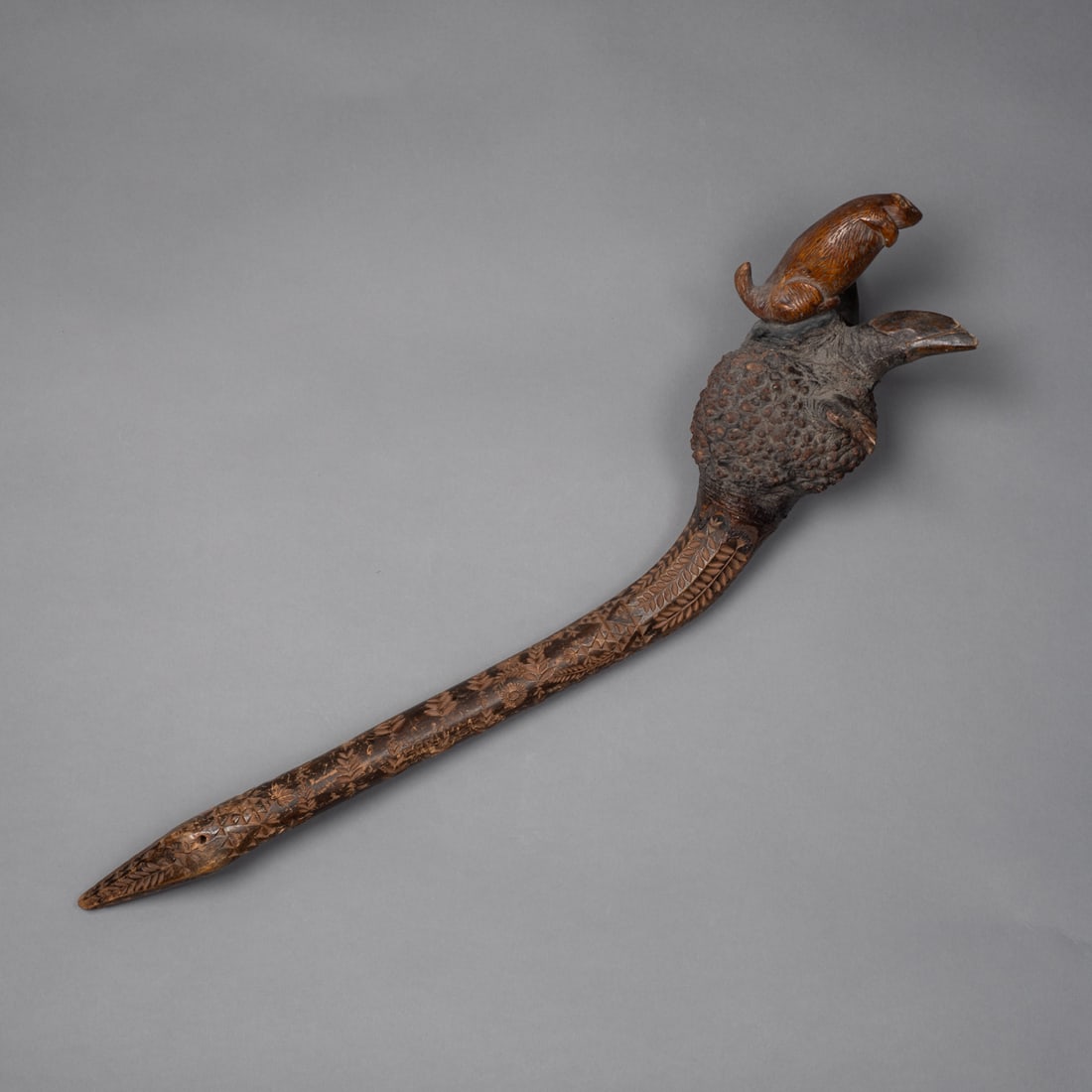 A Northeast carved wood effigy club: Penobscot, 19th century, the long handle fully decorated with foliate chip carving, the head with three spurs and a fully carved animal, possibly a beaver atop. Lg. 21 in. Provenance: Private