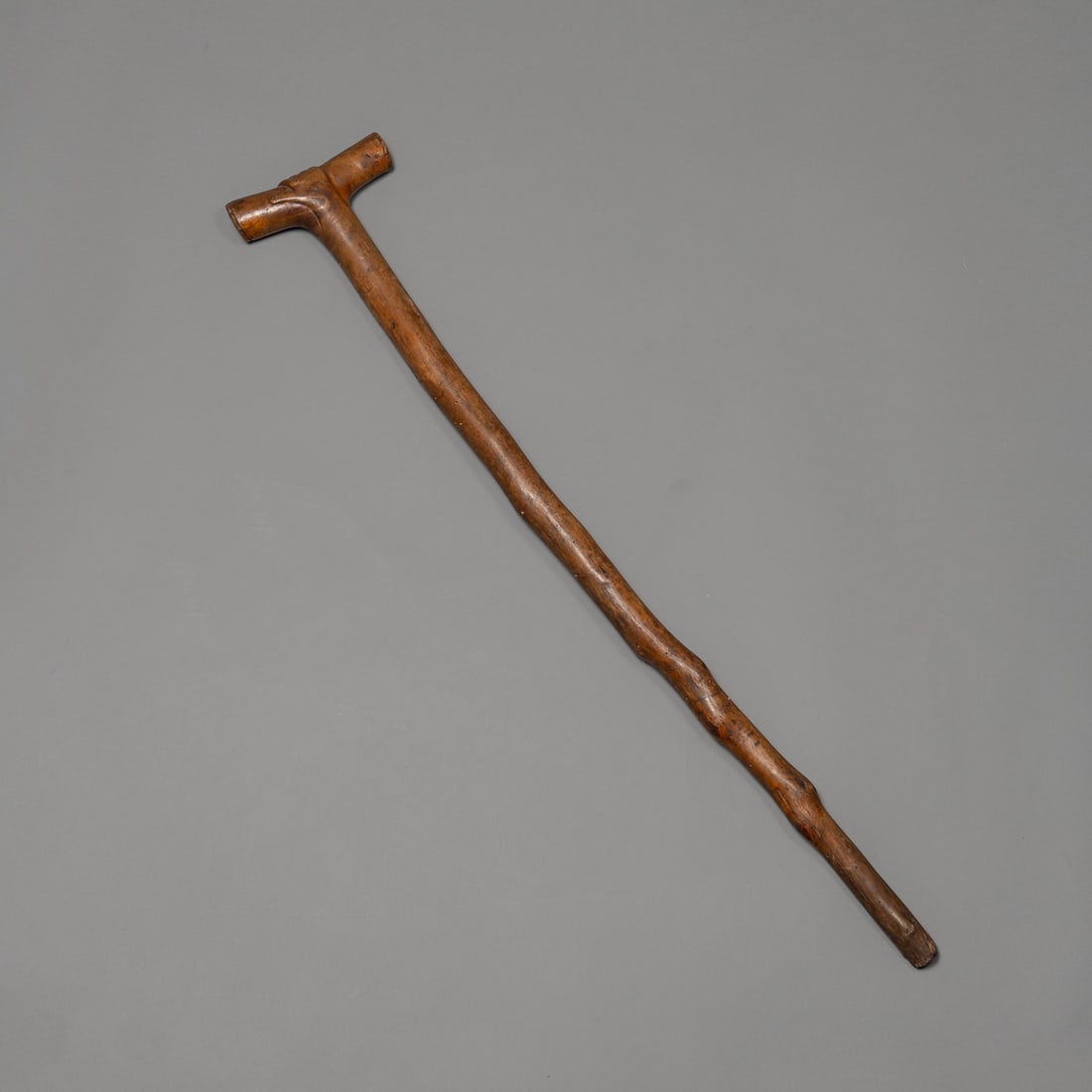 An Iroquois orator's staff: Carved hardwood maple effigy orator' staff depicting hand holding traditional native game piece or treaty scroll, Iroquois people, with naturally curved shaft. The head terminates in a blunt striking