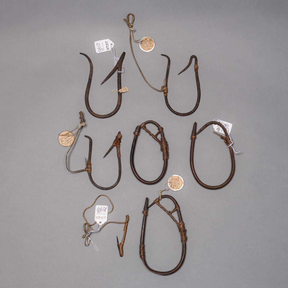 A collection of seven Northwest Coast Halibut hooks: 19th century, each crafted from bent wood with sharp points, the ovular forms each containing fiber wrapping, retaining original patina from age and use. Several have old collection and Skinner