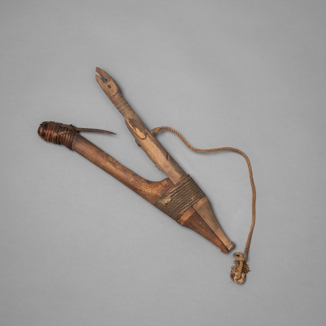 A Northwest Coast Halibut hook: 19th century, formed of a bent wooden shank and a barbed bone point bound together with twisted fiber cord. The piece retains its original surface with a deep, aged patina and tightly wrapped cordage.