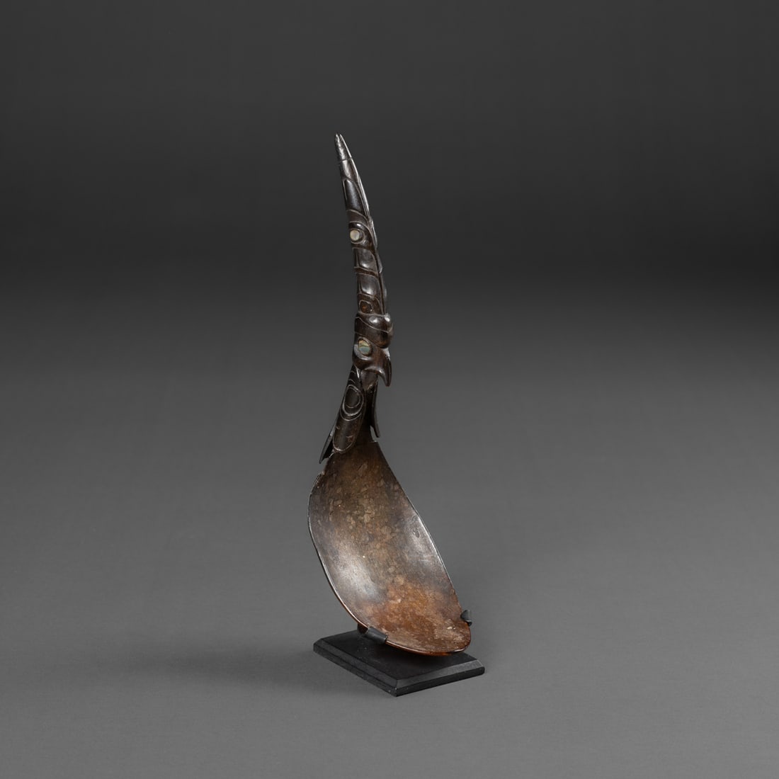 A Northwest Coast horn spoon: 19th century, the carved horn scoop attached to the horn handle with metal nails, the handle with an ornately carved eagle, with carved wings and tail feathers, the eyes inset with shell, with