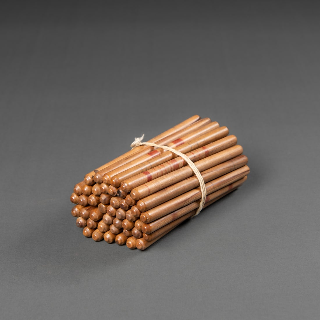 A collection of Northwest Coast game sticks: 19th century, the carved wooden sticks with rounded ends and subtle red banding, tied together with a cord. Each approximately 5 ¼ in.