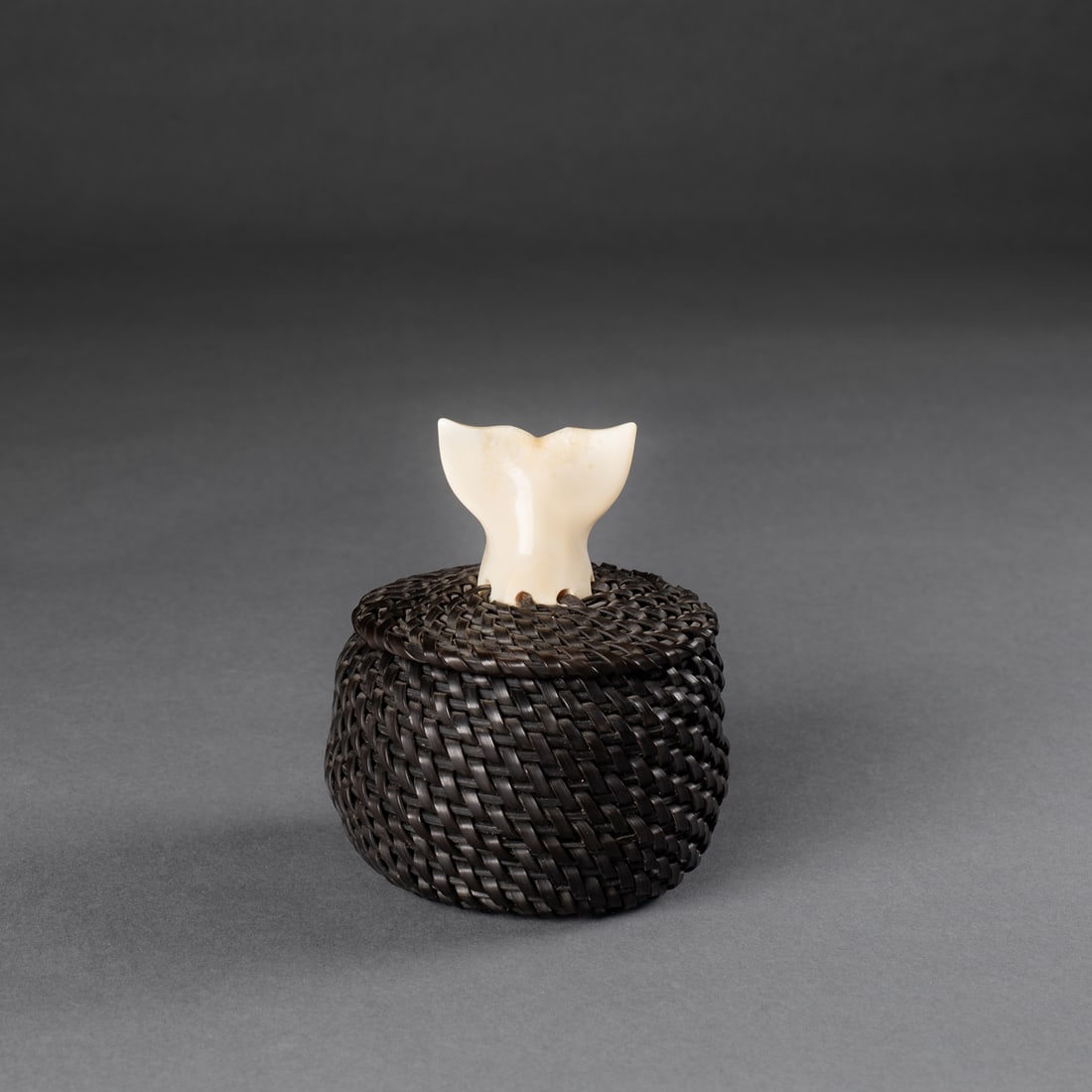 A John Omnik baleen basket: A finely coiled, dark baleen basket of circular form with a carved finial depicting a whale’s flukes emerging upward in a graceful arc. Signed on the inside “John Omnik, Pt. Hope, AK." Ht. 4