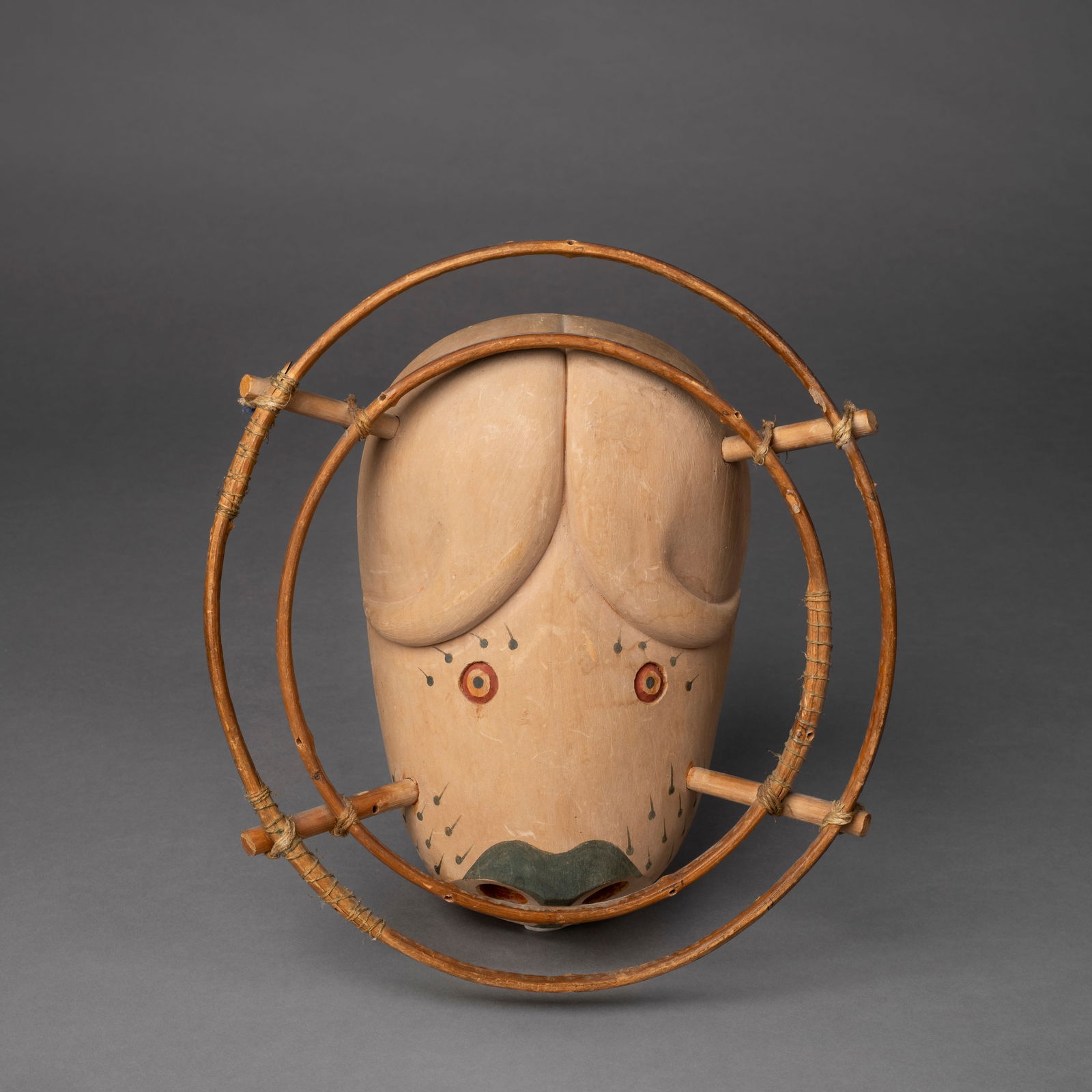 An Eskimo mask: Nunivak Island, in the form of a musk ox, with horns, round eyes and drilled round nostrils, with a double hoop for attachments, dated 1954, signed by Nilsen. Hoop dia. 11, mask size 10 ¼ x 6