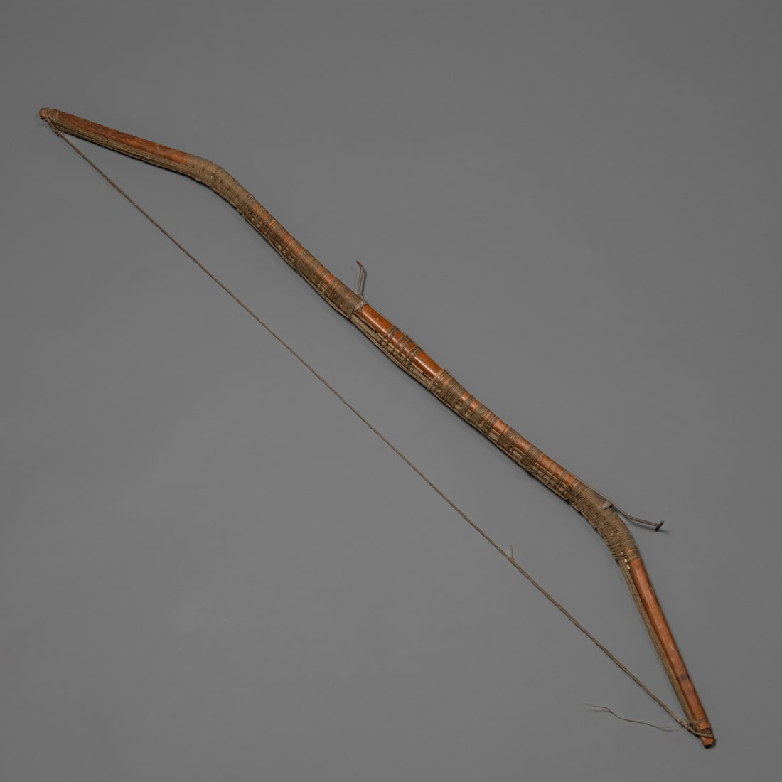 An Eskimo sinew-backed bow: 19th century, the hardwood bow bent at each end, with hide strengtheners and sinew backing and lashing and bow string, with custom wall mount. Lg. 49 in.